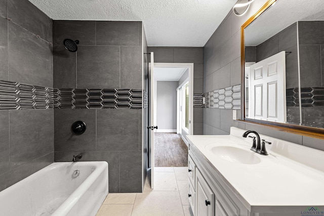 bathroom with a textured ceiling, tiled shower / bath combo, tile patterned flooring, vanity, and tile walls