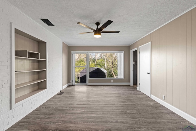 interior space with ceiling fan, dark hardwood / wood-style floors, wooden walls, built in features, and ornamental molding