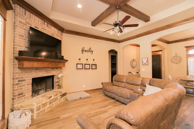 living room featuring ceiling fan, a fireplace, ornamental molding, and light wood-type flooring