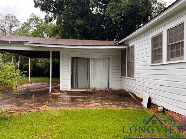 doorway to property with a carport and a lawn