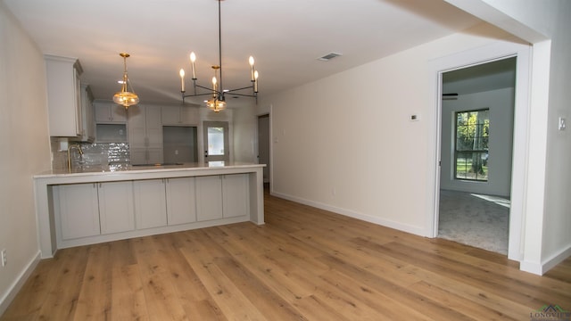 kitchen with decorative backsplash, light wood-type flooring, pendant lighting, a chandelier, and gray cabinets