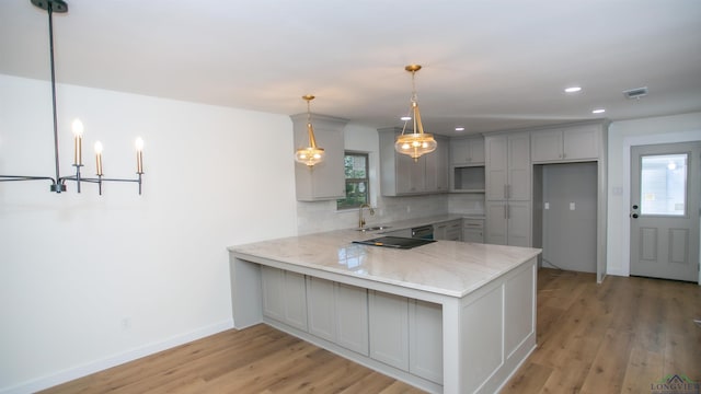 kitchen featuring gray cabinetry, light hardwood / wood-style flooring, kitchen peninsula, decorative light fixtures, and decorative backsplash