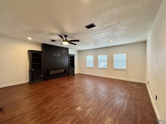 unfurnished living room featuring dark hardwood / wood-style flooring, a textured ceiling, a large fireplace, and ceiling fan