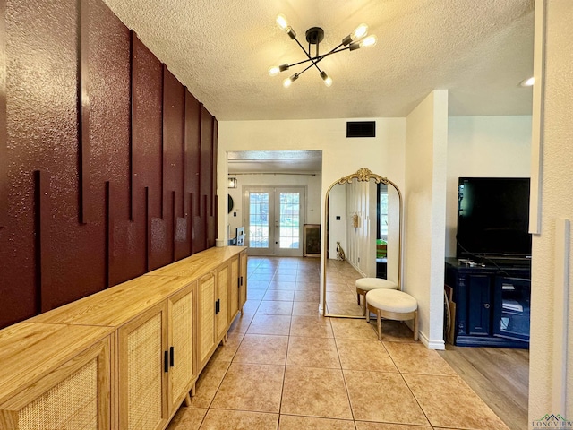 corridor featuring light tile patterned floors, a textured ceiling, french doors, and a chandelier