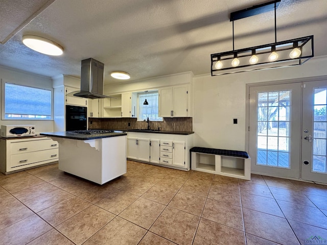 kitchen featuring a kitchen island, island range hood, decorative light fixtures, white cabinetry, and a kitchen bar