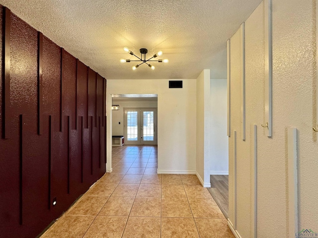 corridor with light tile patterned flooring, a notable chandelier, a textured ceiling, and french doors