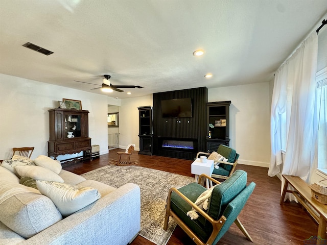 living room featuring ceiling fan, a large fireplace, and dark hardwood / wood-style floors