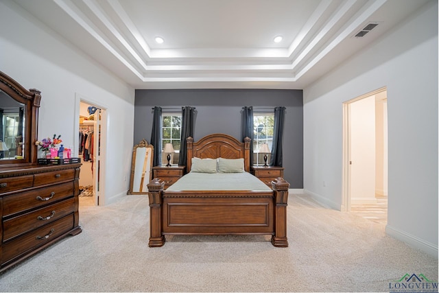 bedroom featuring visible vents, light carpet, a tray ceiling, and a spacious closet