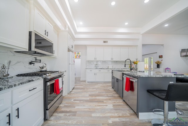 kitchen with white cabinets, light wood finished floors, stainless steel appliances, a sink, and tasteful backsplash