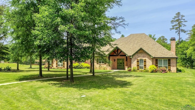 tudor-style house with a chimney, a shingled roof, brick siding, and a front yard