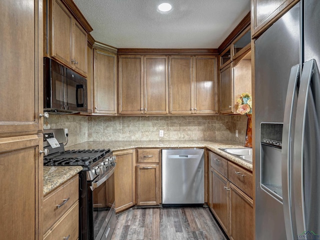 3902 Hazel St, Texarkana, TX 75503 - kitchen with stainless steel appliances, wood finished floors, a textured ceiling, backsplash, and brown cabinets
