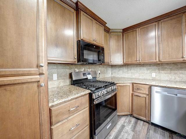 3902 Hazel St, Texarkana, TX 75503 - kitchen featuring appliances with stainless steel finishes, light wood finished floors, decorative backsplash, light stone counters, and a textured ceiling