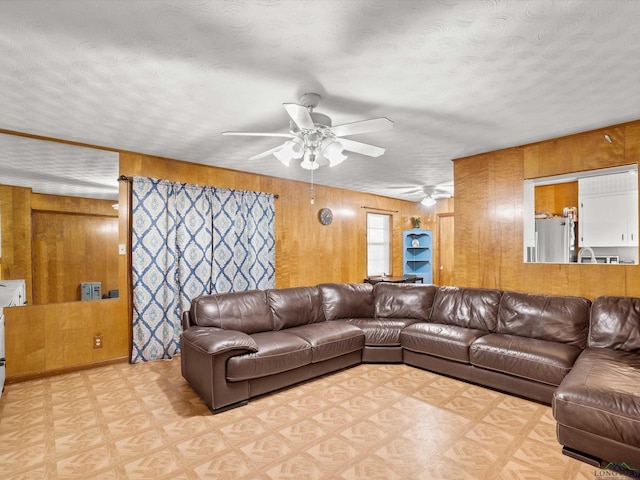 living room featuring a textured ceiling, ceiling fan, and wooden walls