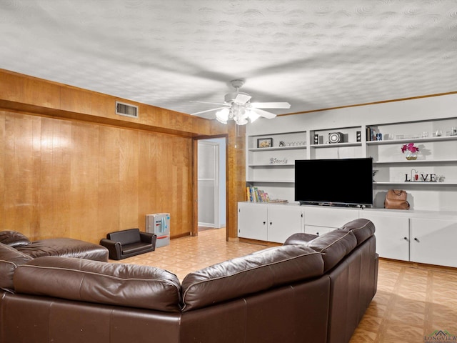 living room featuring ceiling fan, built in features, a textured ceiling, and wooden walls