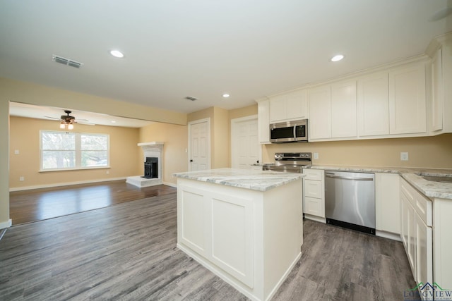 kitchen featuring dark wood-type flooring, appliances with stainless steel finishes, a center island, light stone countertops, and white cabinets