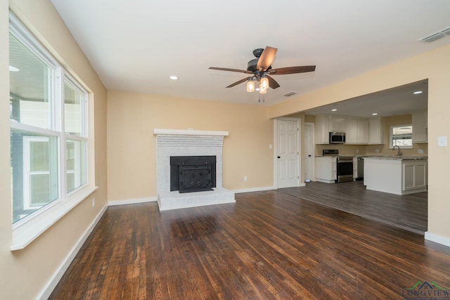 unfurnished living room with a brick fireplace, sink, dark hardwood / wood-style floors, and ceiling fan