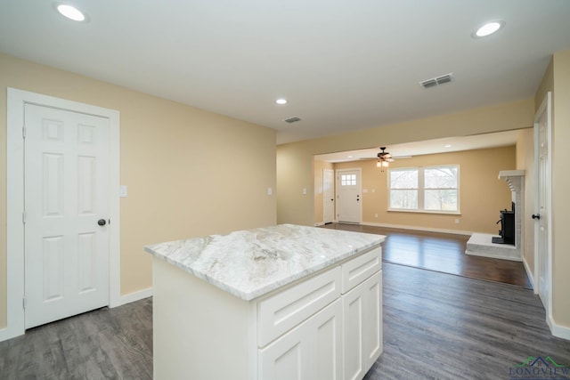 kitchen featuring light stone counters, a fireplace, white cabinets, a kitchen island, and dark hardwood / wood-style flooring