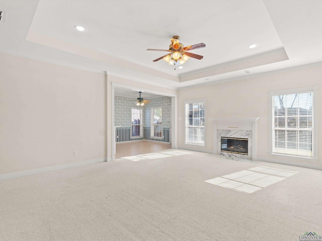 unfurnished living room featuring ceiling fan, ornamental molding, a fireplace, and a tray ceiling