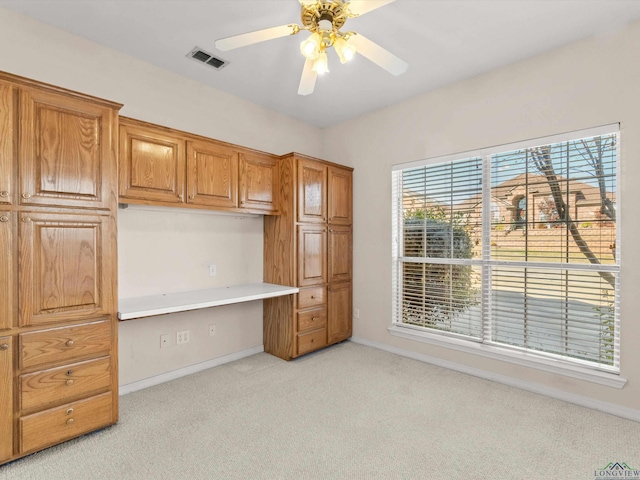 unfurnished office featuring ceiling fan, built in desk, and light carpet