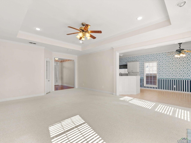 unfurnished living room with a raised ceiling, ceiling fan, carpet, and ornamental molding