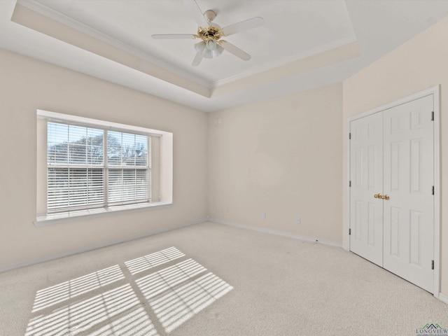 unfurnished bedroom featuring light carpet, ornamental molding, a tray ceiling, ceiling fan, and a closet