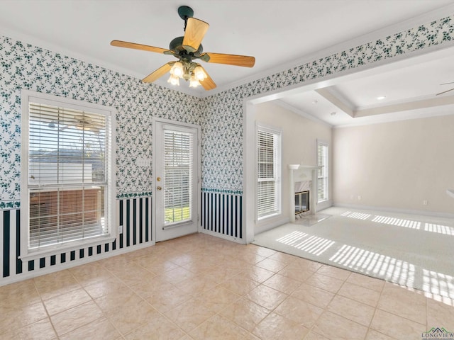 unfurnished living room featuring a high end fireplace, a raised ceiling, ceiling fan, ornamental molding, and light tile patterned flooring