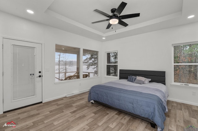 bedroom featuring light hardwood / wood-style flooring, ceiling fan, and a tray ceiling