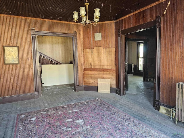 spare room with dark hardwood / wood-style flooring, an inviting chandelier, radiator, and wooden walls