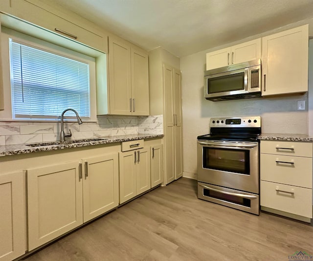 1407 E US-80, White Oak, TX 75693 - kitchen with stainless steel appliances, a sink, light wood-style flooring, tasteful backsplash, and light stone countertops