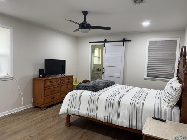 bedroom featuring baseboards, light wood-style flooring, ceiling fan, a barn door, and connected bathroom