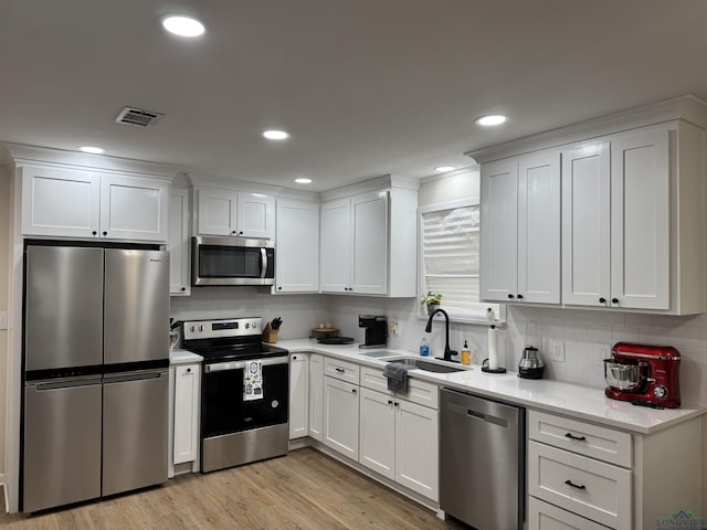 kitchen featuring light wood finished floors, visible vents, appliances with stainless steel finishes, white cabinets, and a sink