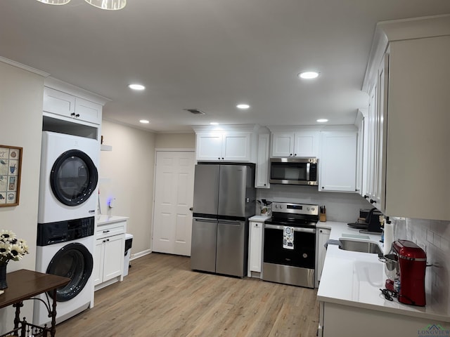 kitchen with visible vents, stainless steel appliances, light countertops, stacked washer and dryer, and white cabinetry