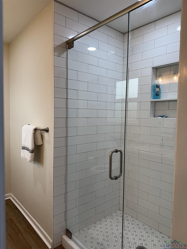 bathroom featuring baseboards, wood finished floors, and a shower stall