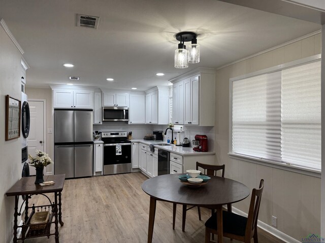 kitchen with visible vents, ornamental molding, stacked washing maching and dryer, stainless steel appliances, and a sink