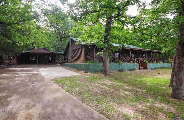 325 Laurel Ln, Holly Lake Ranch, TX 75765 - view of front of house with covered porch, log siding, concrete driveway, a carport, and a front lawn