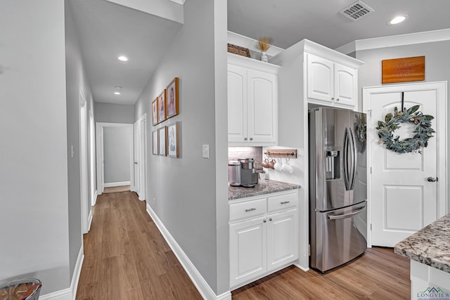 kitchen with visible vents, light wood-style flooring, decorative backsplash, white cabinetry, and stainless steel fridge