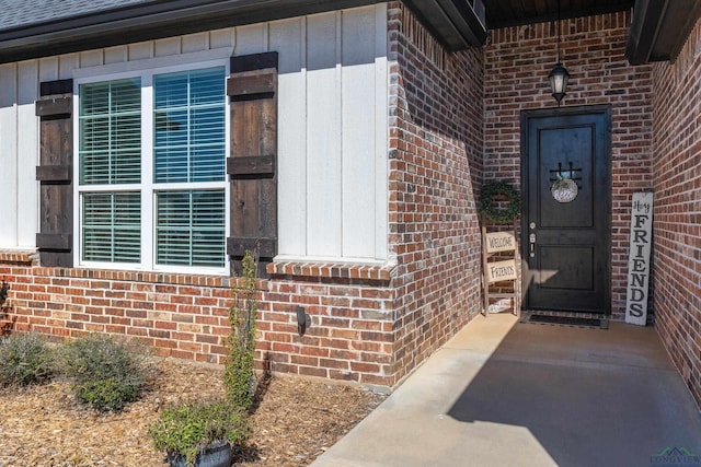 view of exterior entry featuring brick siding and board and batten siding