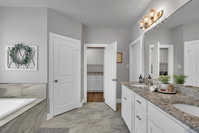 bathroom featuring tiled bath, marble finish floor, a sink, and double vanity