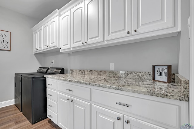 clothes washing area featuring baseboards, cabinet space, light wood finished floors, and washing machine and clothes dryer