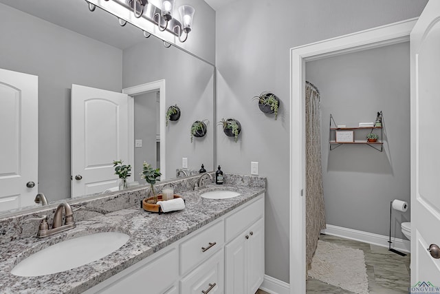 full bathroom featuring double vanity, a sink, toilet, and baseboards