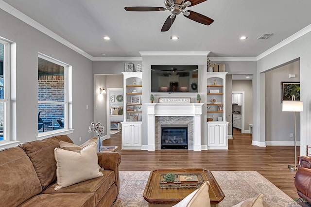 living area featuring baseboards, visible vents, wood finished floors, crown molding, and a high end fireplace