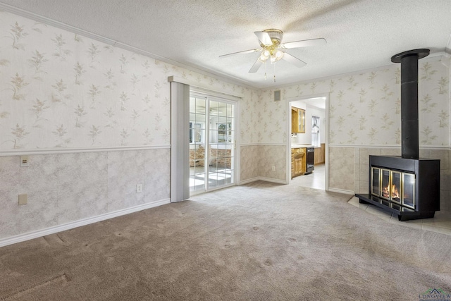 unfurnished living room featuring a textured ceiling, ceiling fan, a wood stove, and light carpet