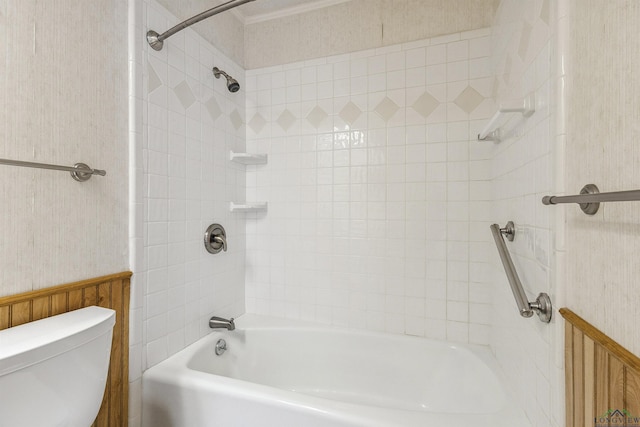 bathroom featuring toilet, tiled shower / bath, and wood walls