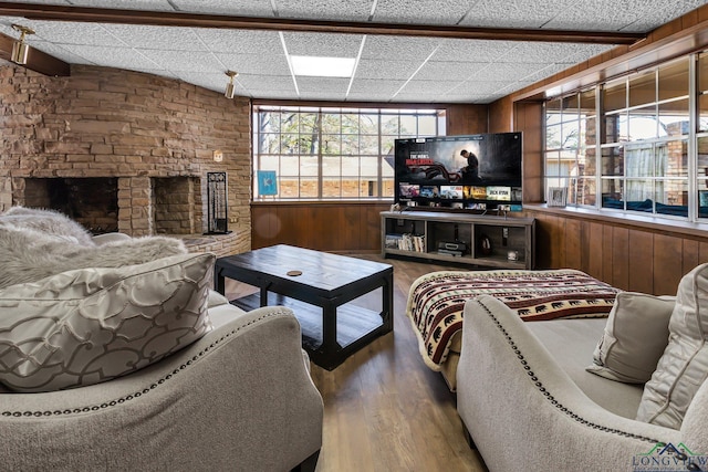 living room with a paneled ceiling, a fireplace, wooden walls, and wood finished floors