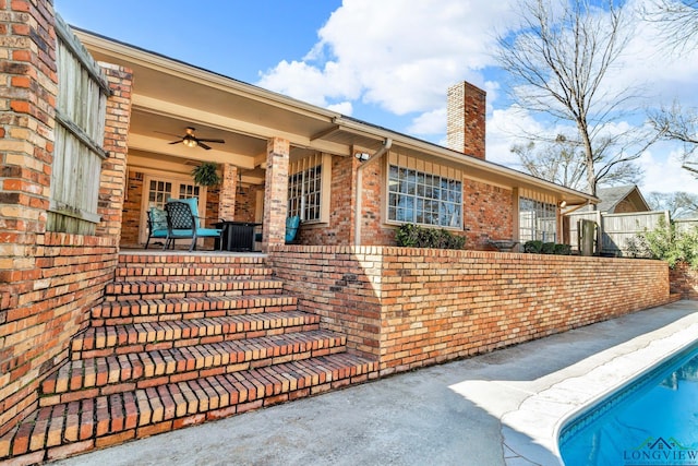 doorway to property with a patio, a chimney, a ceiling fan, and brick siding