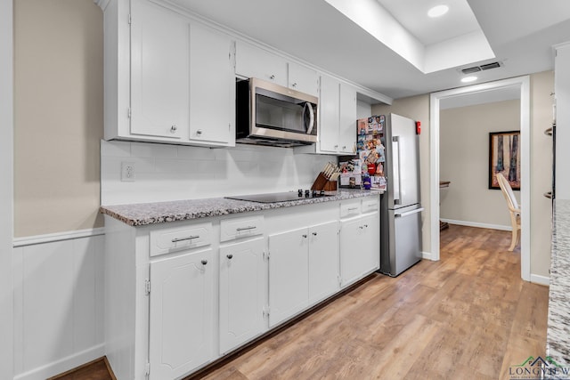 kitchen with light wood finished floors, stainless steel appliances, tasteful backsplash, visible vents, and white cabinetry