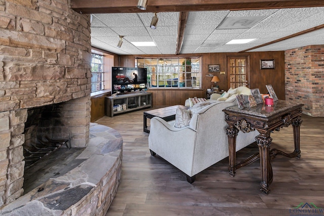 living area featuring a drop ceiling, wood walls, a fireplace, and wood finished floors