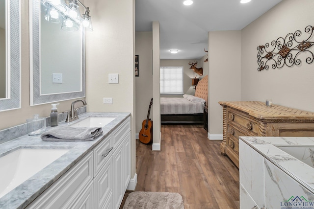 ensuite bathroom featuring double vanity, connected bathroom, a sink, and wood finished floors