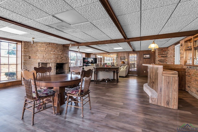 dining area with wood walls, a fireplace, dark wood-style floors, a bar, and beamed ceiling