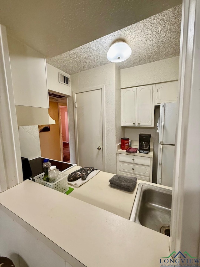 kitchen featuring white cabinetry, white fridge, and a textured ceiling